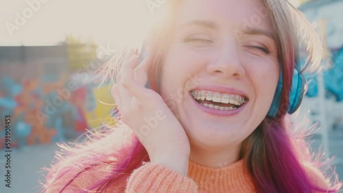 Portrait of a young laughing girl with braces listening to music in headphones in the summer on the street