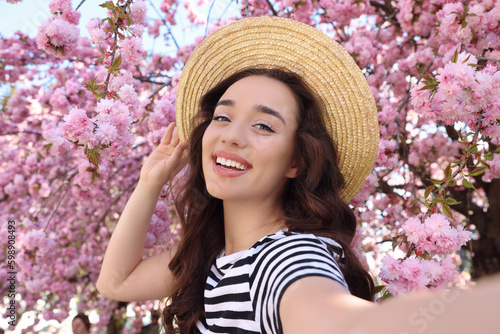 Beautiful woman taking selfie near blossoming sakura tree on spring day