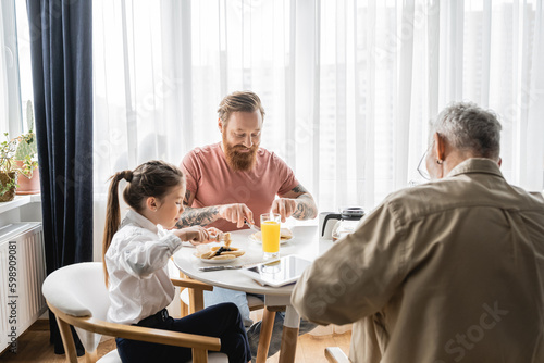 Adopted girl having breakfast with gay parents at home. 