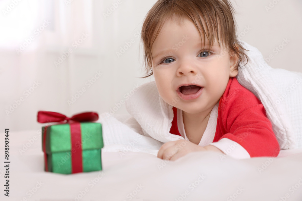 Cute baby wearing festive Christmas costume with gift box in crib, closeup