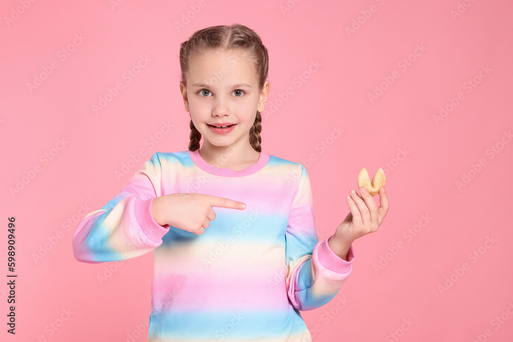 Girl pointing at tasty fortune cookie with prediction on pink background Girl pointing at tasty fortune cookie with prediction on pink background