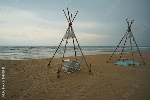 A wooden teepee style with a set of tables and chairs on the beach.