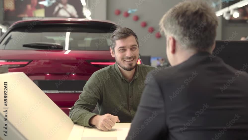 man with beard in car dealership speaks with manager with car on background man with beard in car dealership speaks with manager with car on background