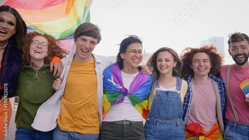 Group of young cheerful friends strolling together on day of gay pride parade in city. People LGBT community pose hugging looking smiling at camera outdoor. Generation z and sexual