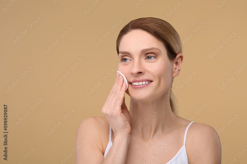 Beautiful woman removing makeup with cotton pad on beige background, space for text Beautiful woman removing makeup with cotton pad on beige background, space for text