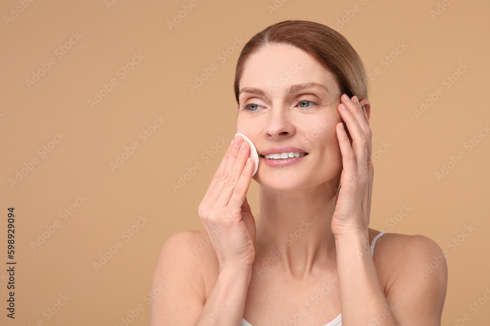 Beautiful woman removing makeup with cotton pad on beige background, space for text Beautiful woman removing makeup with cotton pad on beige background, space for text