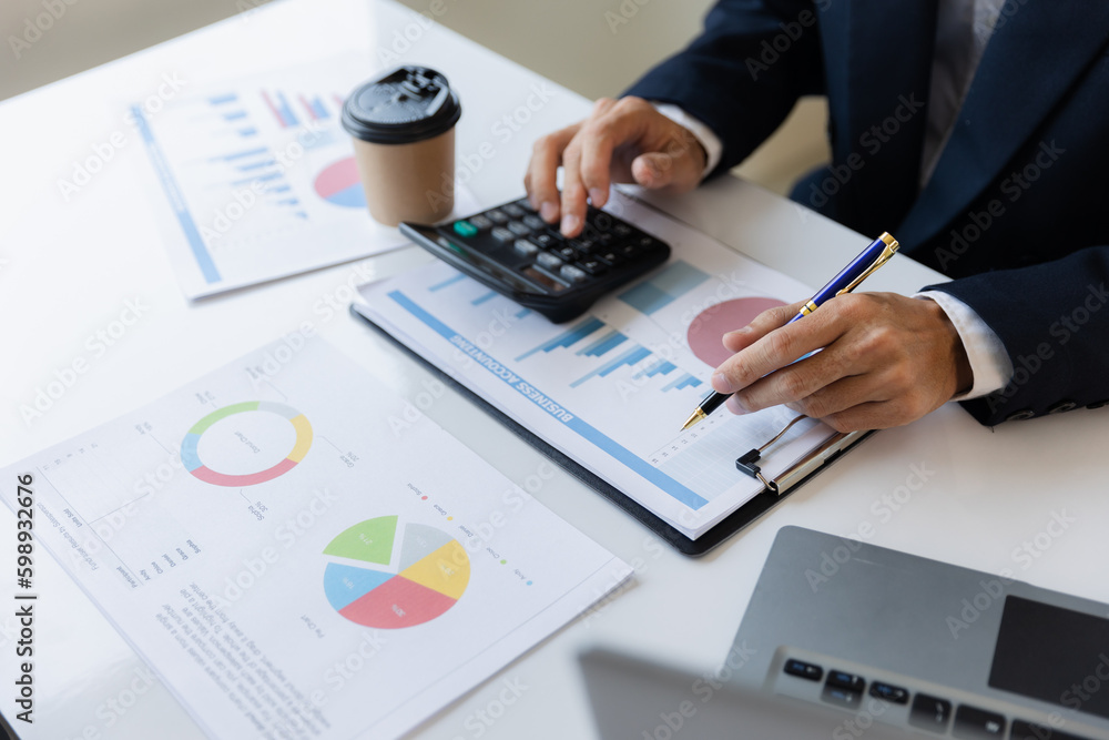 A business man working on a laptop comparing details from graphs Business income chart in real estate, tax, management, marketing, technology in private office. A business man working on a laptop comparing details from graphs Business income chart in real estate, tax, management, marketing, technology in private office.