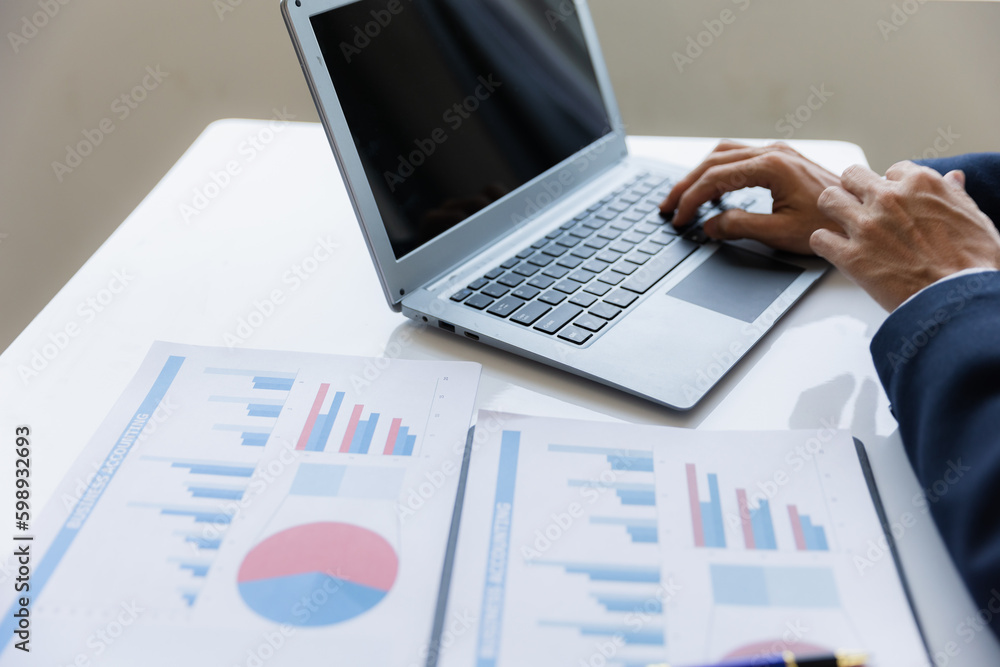 A business man working on a laptop comparing details from graphs Business income chart in real estate, tax, management, marketing, technology in private office. A business man working on a laptop comparing details from graphs Business income chart in real estate, tax, management, marketing, technology in private office.