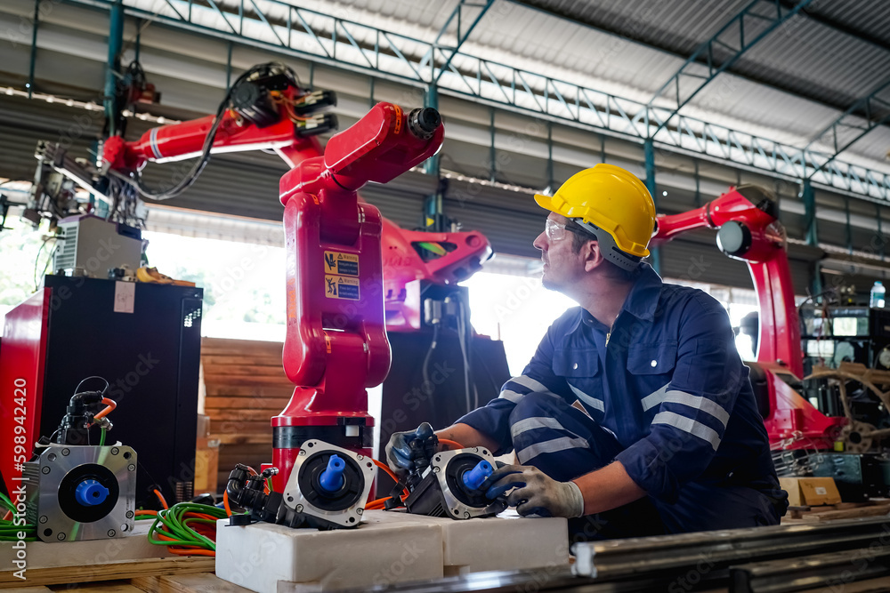 Male technician programs a robot arm with a digital tablet and assembly robot in a factory. Apprentice engineers programming robots in factory. Male technician programs a robot arm with a digital tablet and assembly robot in a factory. Apprentice engineers programming robots in factory.