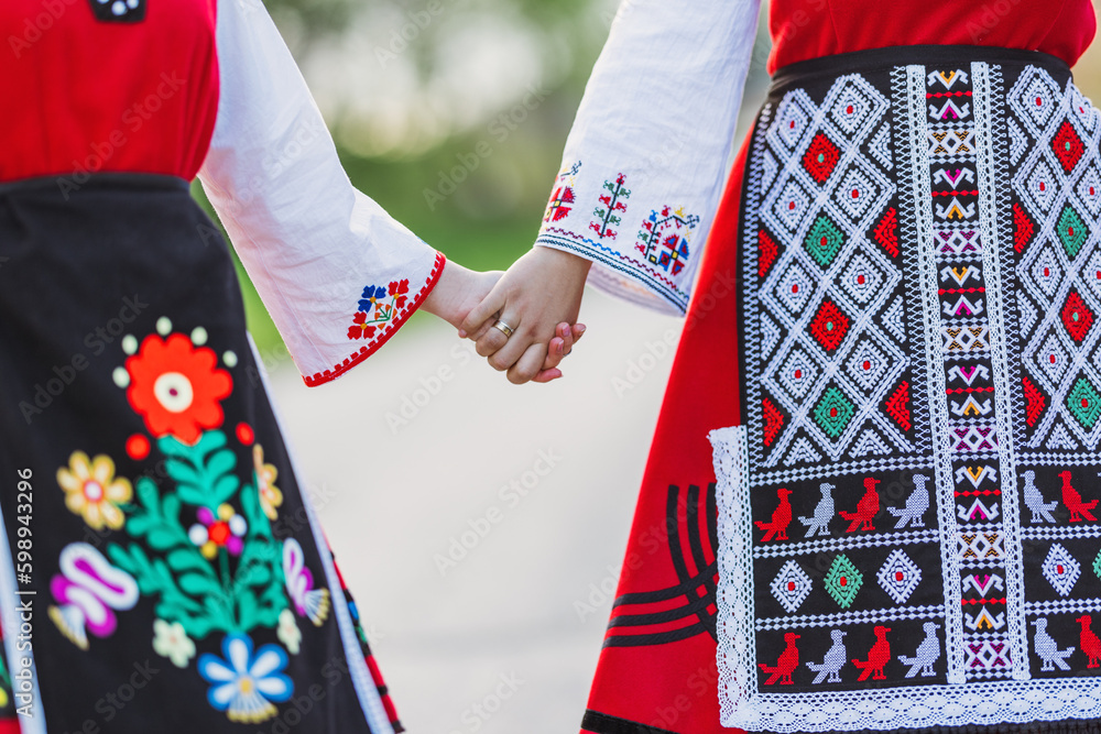 Girls in traditional bulgarian ethnic costumes with folklore embroidery holding hands. The spirit of Bulgaria - culture, history and traditions. - obrazy, fototapety, plakaty 