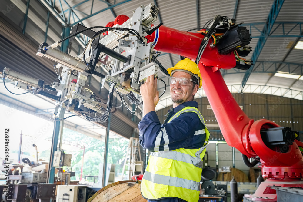 Male technician programs a robot arm with a digital tablet and assembly robot in a factory. Apprentice engineers programming robots in factory. Male technician programs a robot arm with a digital tablet and assembly robot in a factory. Apprentice engineers programming robots in factory.