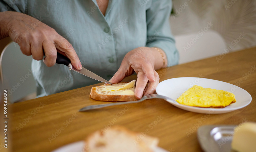 the hands of an elderly Caucasian woman spread bread with butter during a delicious and nutritious breakfast in the family circle.