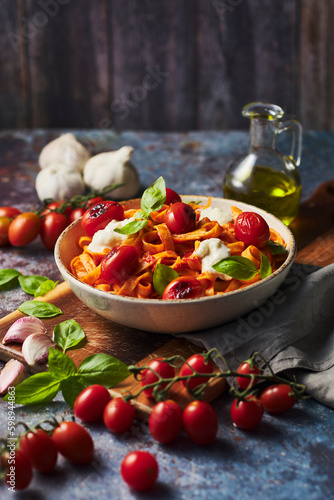 Delicious pasta dish with tomatoes and fresh basil. Cherry tomatoes and fresh mozzarella cheese on homemade pasta. Italian food with garlic and olive oil. 