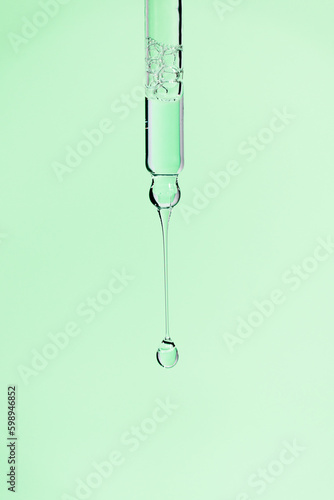 Transparent pipette with facial serum and falling drop on green background. Skin care cosmetic product with bubbles closeup. Anti aging serum with retinol in glass dropper. Essential oil or gel macro. © gorina_anna