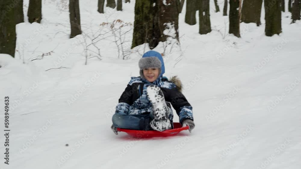 Young boy joyfully sledging down a snowy hill on his plastic sled. The snowy landscape, winter holidays and outdoor activities Young boy joyfully sledging down a snowy hill on his plastic sled. The snowy landscape, winter holidays and outdoor activities