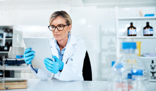Detailing the process of her experiments. a mature scientist using a digital tablet in a lab.