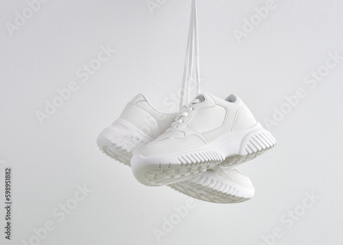 Pair of classic sneakers or trainers hanging on white wall. Casual lifestyle. Fashionable sports shoes. Creative minimalistic layout with footwear mock up for your design. Advertising for shoe store photo