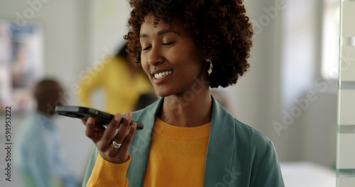 Young businesswoman talking on over her phone's speaker at the entrance of an office boardroom with colleagues meeting in the background