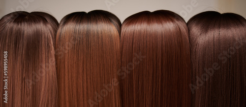 Showcase of natural looking wigs in different shades of brunette fixed on the wig holders in beauty salon. Row of mannequin heads with variation colors hair on shelf in wig shop