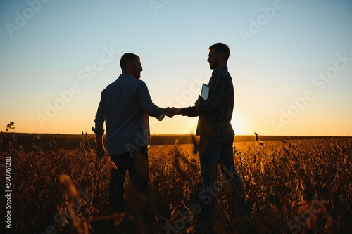 Two farmers shaking hands in soybean field.