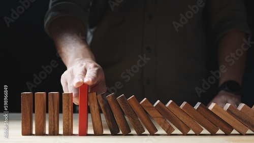 Businessman hand stopping wooden domino business crisis effect or risk protection on dark background. Concept of Risk, Risk Management, Assessment, Business, Crisis, Financial, Planning, Economic
