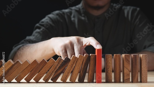 Businessman hand stopping wooden domino business crisis effect or risk protection on dark background. Concept of Risk, Risk Management, Assessment, Business, Crisis, Financial, Planning, Economic