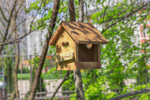 A wooden bird feeder on a background of young green leaves. Beautiful nature wallpaper, outdoor