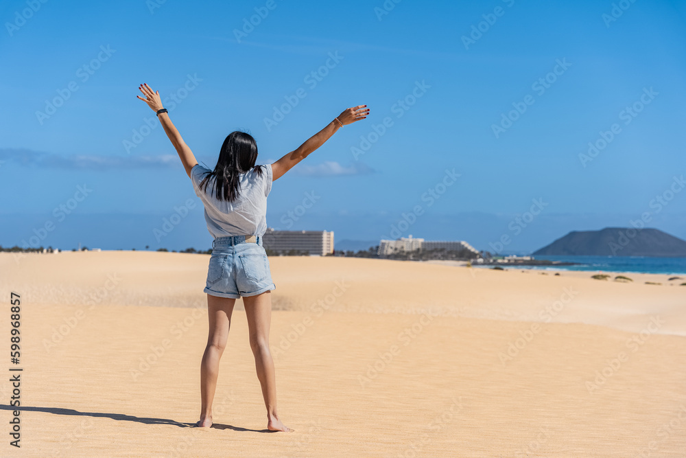 Mujer de espalda con brazos abiertos extendidos en arena amarilla con cielo azul Mujer de espalda con brazos abiertos extendidos en arena amarilla con cielo azul