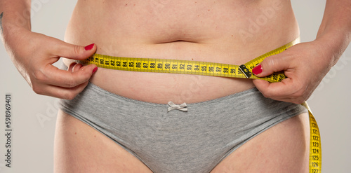 Close up of females fat belly and a measuring tape, isolated.