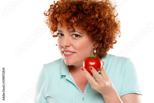 Portrait of a curly red hair woman holding a tomato, cut out on white background.