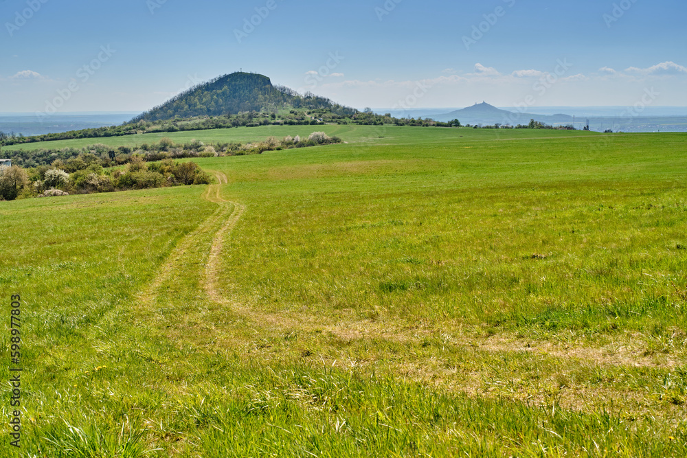 Pasture grazing land in scenic nature with view of Central Bohemian Highlands (Czech: České Středohoří) mountains of Radobyl and Hazmburk castle. Popular natural reservation and holiday destination. Pasture grazing land in scenic nature with view of Central Bohemian Highlands (Czech: České Středohoří) mountains of Radobyl and Hazmburk castle. Popular natural reservation and holiday destination.
