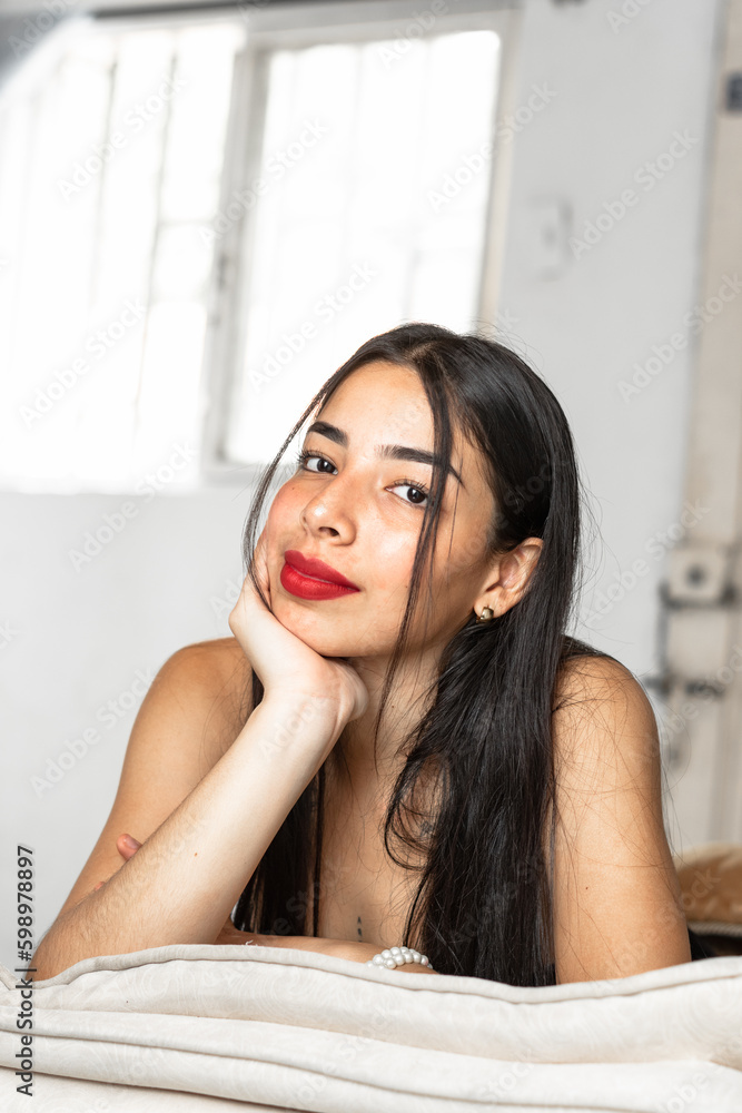 beautiful latina teenager with dark skin, lying on the furniture of her house looking straight ahead.