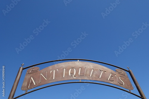 Old advertisement sign with the French text "Antiques" against clear blue sky