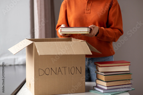 charity, donation and volunteering concept - young woman puts books in cardboard box at home photo