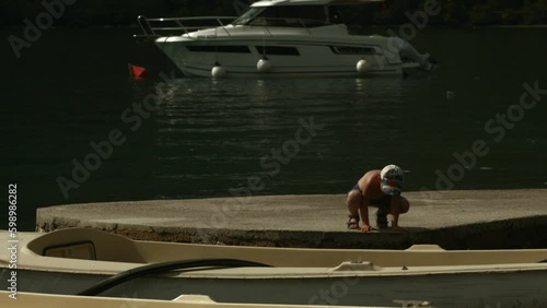Boy walking on wooden pier along the yachts. Creative. Little boy spending time near the lake. Generative AI photo