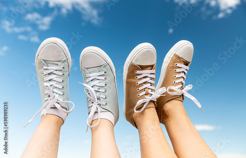 footwear, summer and people concept - close up legs in lace-up shoes upside down over blue sky