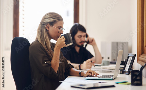 She has that make-it-happen mindset. a young businesswoman working on a laptop in an office with her colleague in the background.