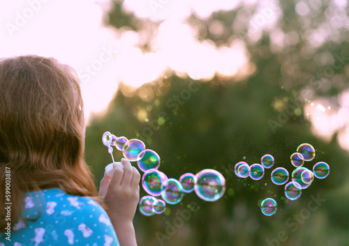 girl blowing soap bubbles, abstract blurred natural background. rear view. dreaming, harmony peaceful atmosphere. Happy childhood concept. template for design