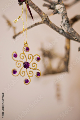 Golden hanging ornament with purple gems on a wooden branch as Christmas decoration. Natural wood and intricate shiny ornament.