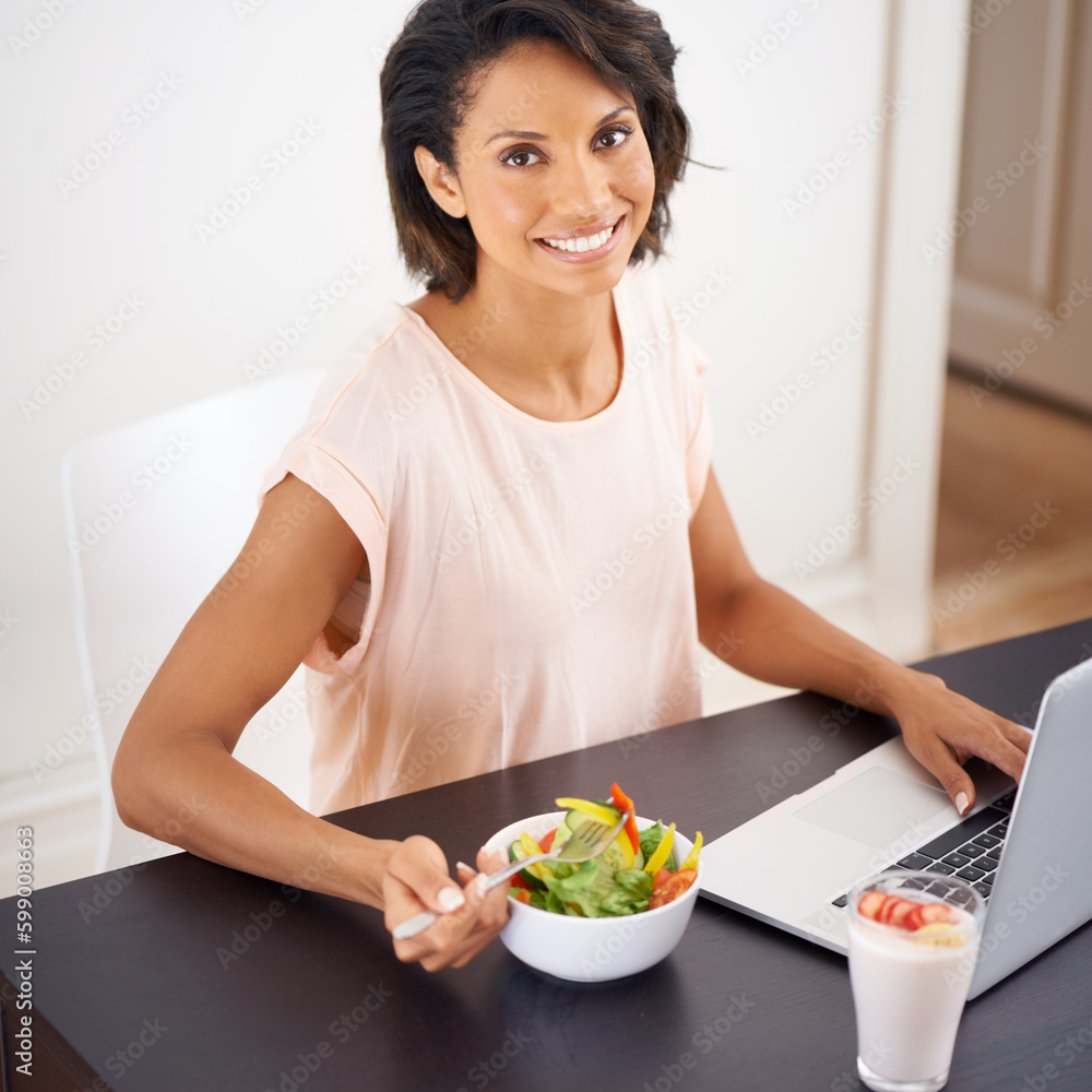 Satisfying and healthy lunch at home. Portrait of a young woman enjoying a salad and working on a laptop at home. Satisfying and healthy lunch at home. Portrait of a young woman enjoying a salad and working on a laptop at home.