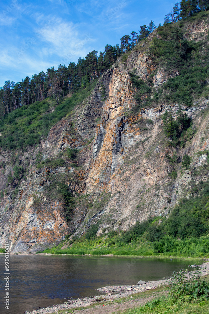 Picturesque rocks covered with coniferous forest against a blue sky with white clouds.