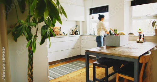 Young woman standing at a table in her kitchen unpacking a box of delivered groceries
