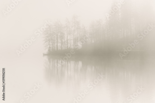 A captivating morning view of Lake Bled in Slovenia, enveloped in dense fog. The shoreline and the canoeing club building emerge from the mist, creating a mystical and serene atmosphere. © Alejandro