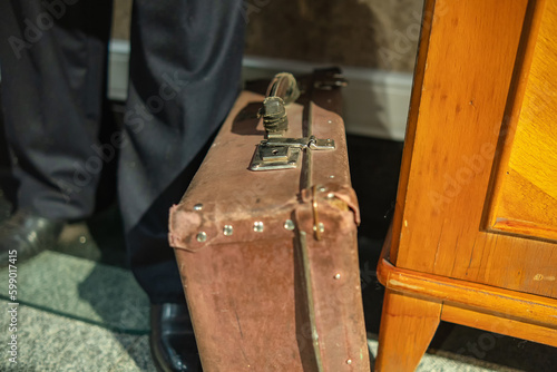 A very old suitcase stands next to a person's foot photo