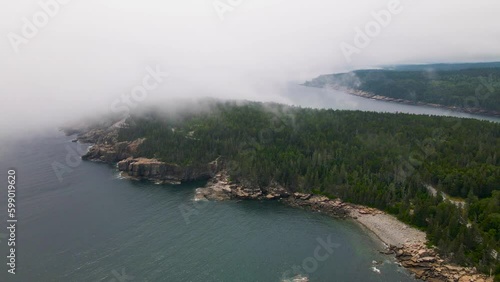 4K Aerial Drone stationary view of clouds rolling in over pine tree peninsula. Water, trees, rocks, clouds visible