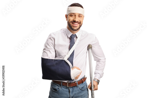 Young man with a broken arm and bandage on head leaning on a crutch and smiling