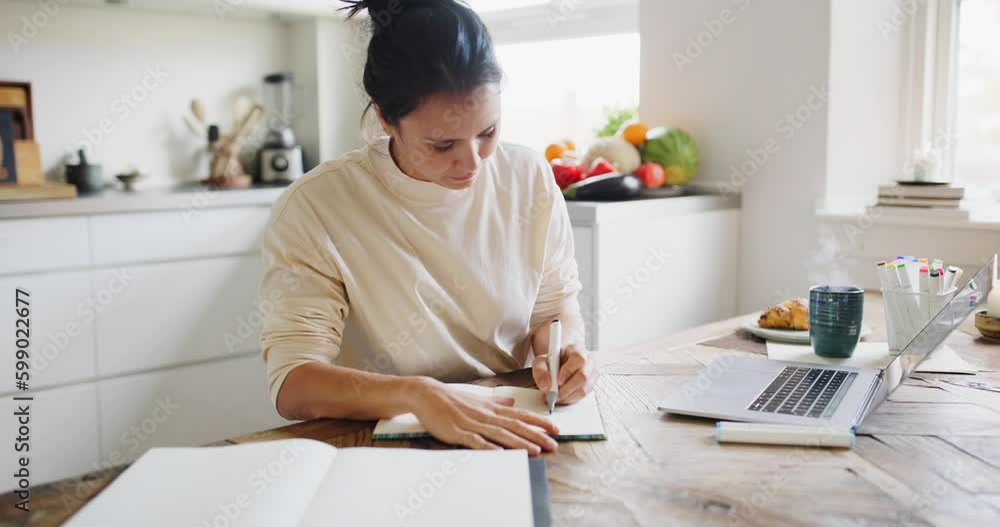 Young woman drawing designs in a sketchbook while sitting at a table in her kitchen at home Young woman drawing designs in a sketchbook while sitting at a table in her kitchen at home