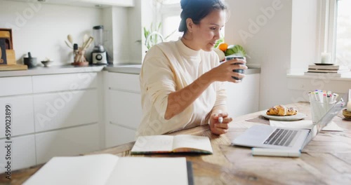 Young woman drinking tea while drawing in a sketchbook and working on a laptop at her kitchen table