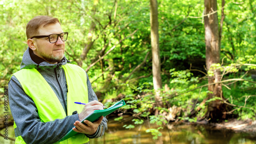 Man ecologist in the forest near a reservoir makes marks of control of the ecological situation of the environment.