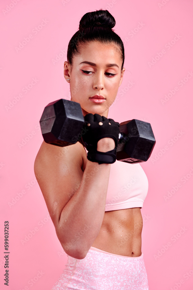 Shes got muscles of steel. Studio shot of a sporty young woman exercising with a dumbbell against a pink background.